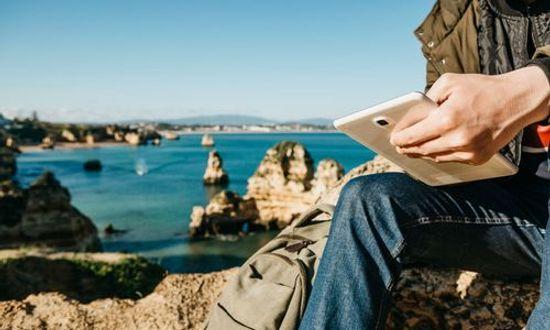 Feature image - A young man or a tourist uses a tablet sitting on the Atlantic coast next to the city called Lagos in Portugal.jpg